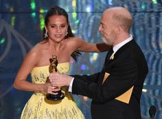 a man in a tuxedo standing next to a woman wearing a yellow dress