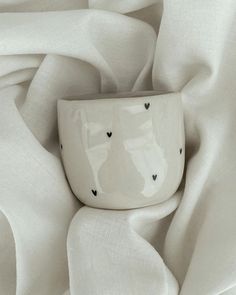 a white cup sitting on top of a table covered in sheets and cloths with hearts drawn on it