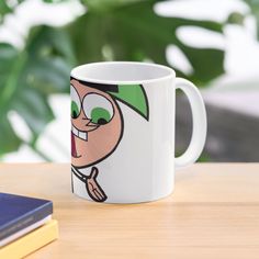 a coffee mug with a cartoon character on it sitting on a table next to a book