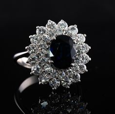 This estate ring is crafted in solid 18K White Gold (carefully tested and guaranteed). The center natural Earth mined oval cut Sapphire measures 9x7mm (2.20 carats). This gem has a deep blue color. It also has a tiny chip that cannot be seen without magnification. The center stone is surrounded with 32 round brilliant cut diamonds. 16 diamonds total 1.28 carats and smaller 16 gems total .64 carats. The grand total diamond weight is 1.92 carats of VS1 clarity and G color. Size 7 (sizable). The ri Elegant Cluster Sapphire Ring, Gia Certified, Elegant Gia Certified Cluster Sapphire Ring, Luxury Oval Gemstone Flower Ring, Fine Jewelry Oval Flower Ring With Halo Setting, Luxury Flower Ring With Halo Setting For Formal Occasions, Oval Flower Ring With Halo Setting, Elegant Gemstone Flower Ring For Formal Occasions, Luxury Formal Flower Ring With Center Stone, Heirloom Diamond Flower Ring, Oval Shaped