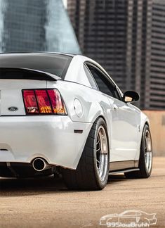 the rear end of a white mustang car parked in front of a tall skyscraper building