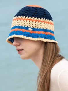 a young woman wearing a crocheted hat by the water with her hair pulled back