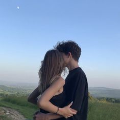 a man and woman kissing in the middle of a grassy field with a moon behind them