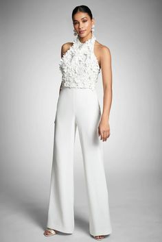 a woman is posing in white pants and a top with flowers on the side,