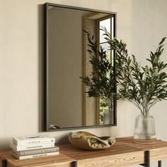 a mirror sitting on top of a wooden table next to a vase filled with plants