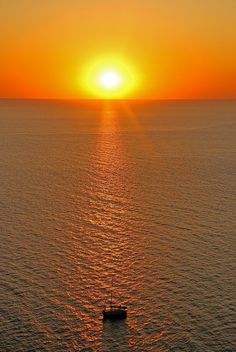 a small boat floating on top of a body of water under a bright orange sky