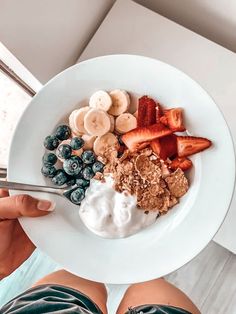 a person holding a bowl of fruit and yogurt on top of a white plate