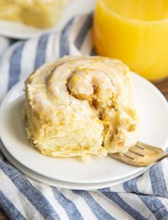 a white plate topped with a cinnamon roll next to a glass of orange juice and a wooden spoon