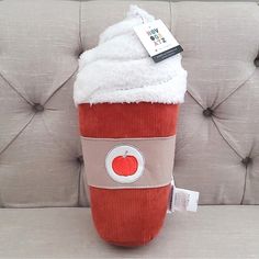 an orange and white stuffed animal sitting on top of a gray couch next to a tag