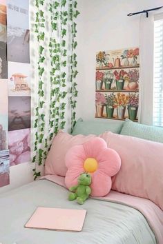 a pink flower sitting on top of a bed next to a green teddy bear and pillows