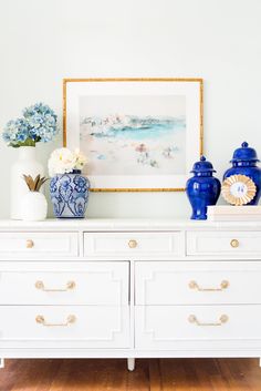 blue and white vases sit on top of a dresser in front of a painting