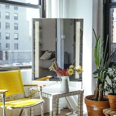 a yellow chair sitting in front of a large mirror on top of a table next to a potted plant