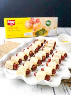 pigs in a blanket on a plate next to a box of mustard