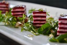 some food that is on a white plate with green leafy greens and red beets