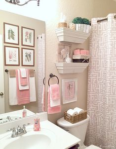 a bathroom decorated in pink and white with pictures on the wall above the toilet, sink, and shower curtain