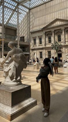 a woman is looking at a statue in a large room with many windows and people walking around