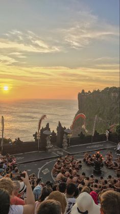 a group of people standing on top of a road next to the ocean at sunset