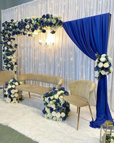 a blue and white wedding set up with flowers on the stage, chairs and drapes