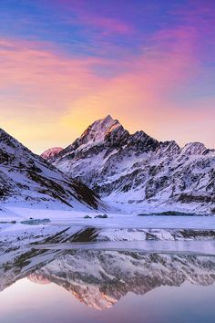 the mountains are covered in snow as the sun is setting over them and reflecting in the water