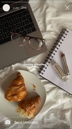 an open laptop computer sitting on top of a bed next to a plate with croissants