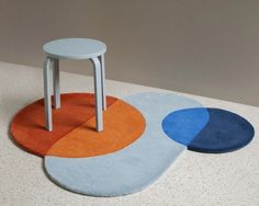 three different colored rugs on the floor with one chair and two stools next to each other