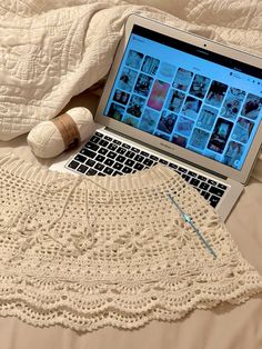 an open laptop computer sitting on top of a bed next to a ball of yarn