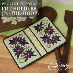 a pot holder with purple flowers on it and a wooden spoon in front of it