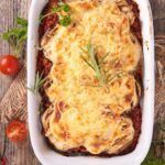 a casserole dish with meat and vegetables in it on top of a wooden table