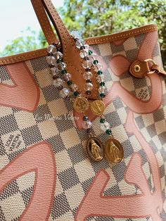 a brown and white handbag with some charms on it's handle, sitting in front of trees