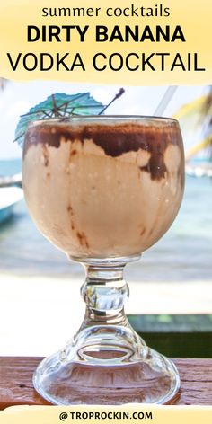 a drink in a glass sitting on top of a wooden table next to the ocean