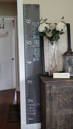 a tall vase with flowers on top of a wooden table next to a growth chart