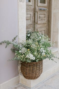 a basket filled with flowers sitting on the side of a building next to a door