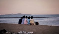 four people sitting on the beach watching the ocean