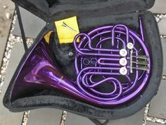 a purple french horn in a black case on the ground with a yellow tag attached to it