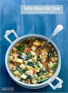 a pot filled with soup and vegetables on top of a blue table next to a spoon