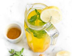 a pitcher filled with lemonade and mint next to some sliced lemons on a white surface