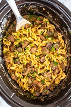 a crock pot filled with pasta and meat in sauce, garnished with parsley