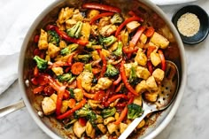 a pan filled with chicken, broccoli and red peppers on top of a table