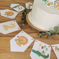 a birthday cake decorated with animal cards on a wooden table next to a leafy garland