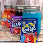 three jars filled with kool aid sitting on top of a wooden table next to each other