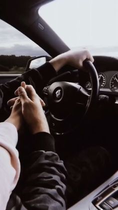 a person driving a car with their hands on the steering wheel, and another hand holding the steering wheel