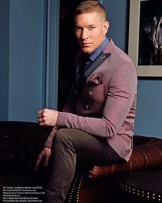 a man sitting on top of a couch wearing a purple suit and blue shirt with his hands in his pockets