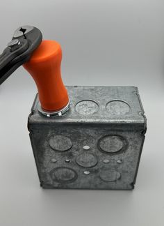 an orange and black tool is on top of a metal box with holes in it