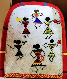 a red and white woven bag with people painted on the front, sitting next to a wall