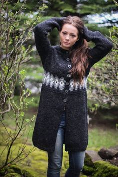 a woman standing in the woods with her hands on her head and wearing a coat