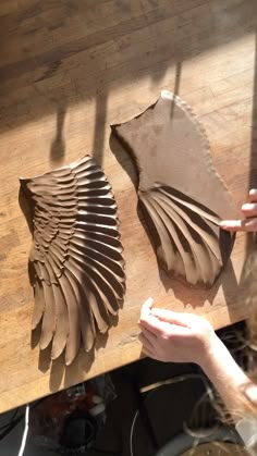 two people are working with clay on a wooden table and one person is holding a piece of paper