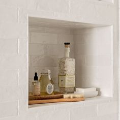 a bathroom shelf with soap, lotion and other personal care items on it in front of a white brick wall