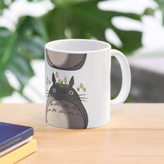 a coffee mug with totoro on it sitting on a table next to some books