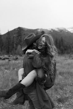 black and white photograph of two people hugging each other in an open field with mountains in the background