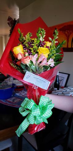 a bouquet of flowers is wrapped in red paper and tied with a green checkered ribbon